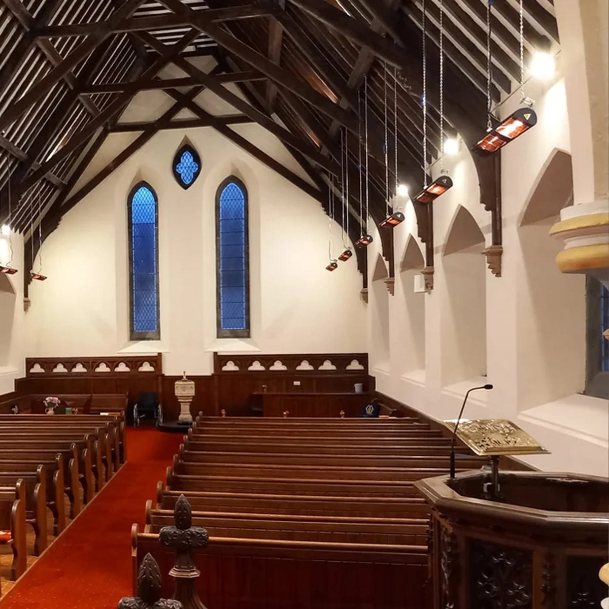 Zwarte MANHATTAN 3000 W verwarmers hangen aan de muren van een kerk.