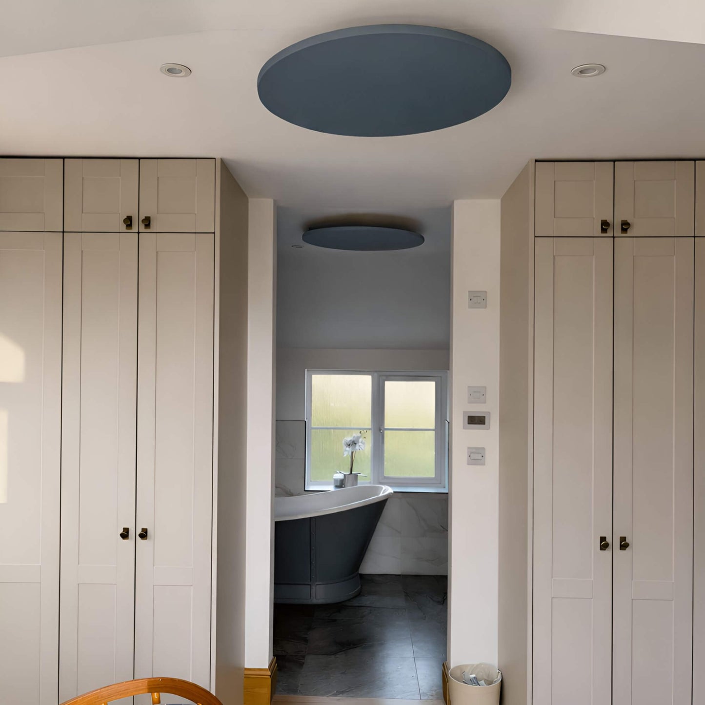 Rond grijs Herschel Select XLS infraroodpaneel gemonteerd aan het plafond in interieur met zicht op badkamer