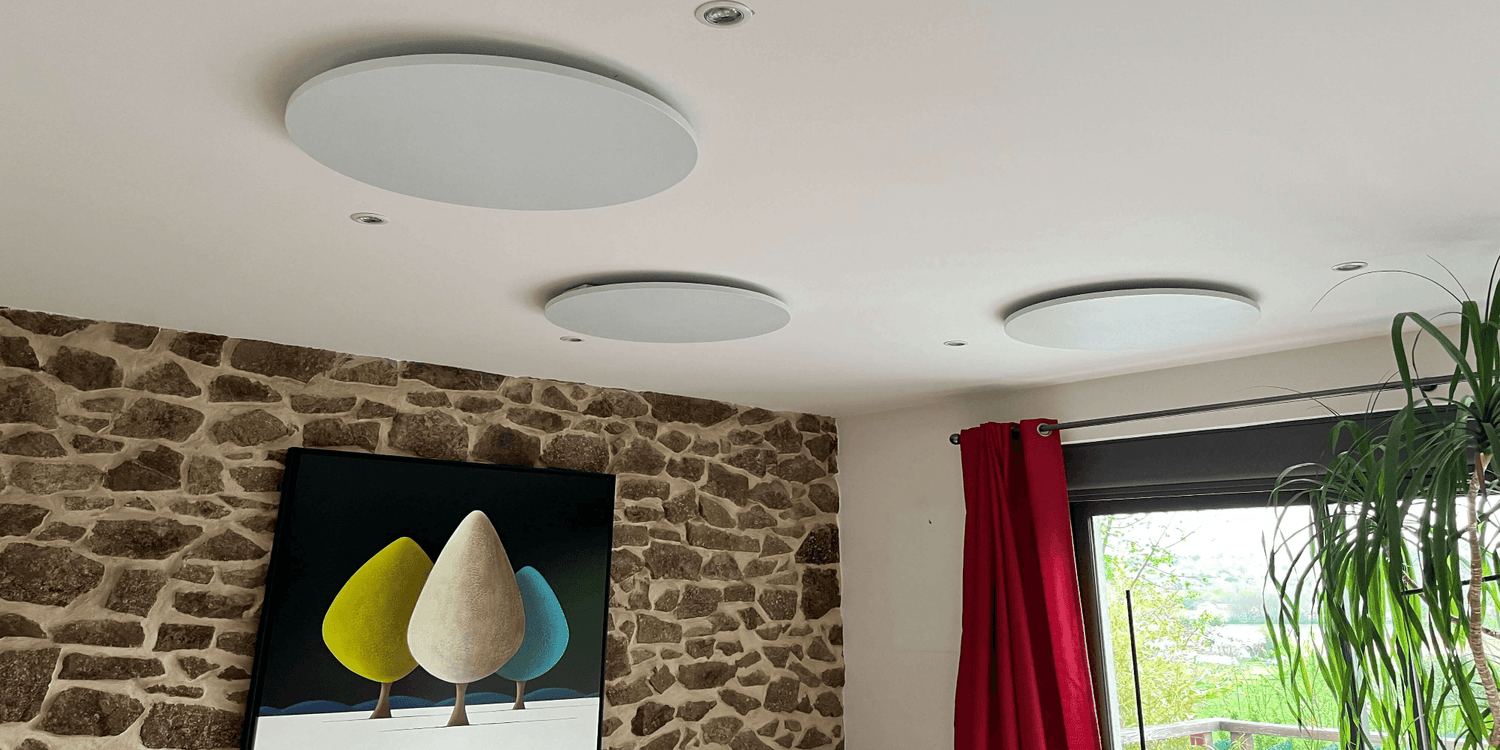 Drie witte ronde Herschel Select XLS infraroodpanelen gemonteerd aan het plafond in een woonkamer met stenen muur en groot raam