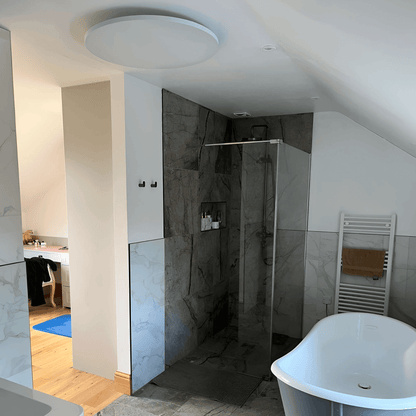 Wit rond Herschel Select XLS infraroodpaneel gemonteerd aan het plafond in een badkamer