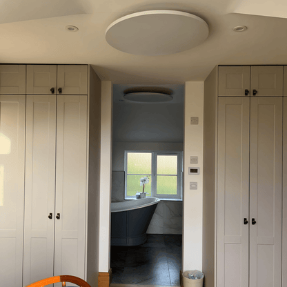 Wit rond Herschel Select XLS infraroodpaneel gemonteerd aan het plafond in een woninginterieur met zicht op badkamer