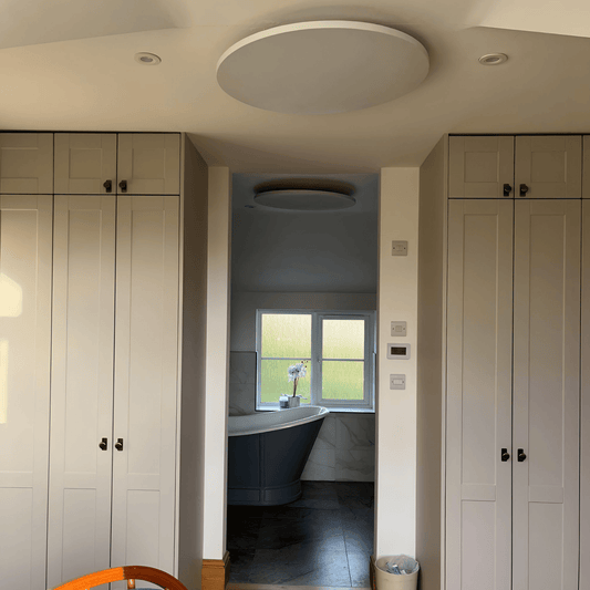 Wit rond Herschel Select XLS infraroodpaneel gemonteerd aan het plafond in een woninginterieur met zicht op badkamer