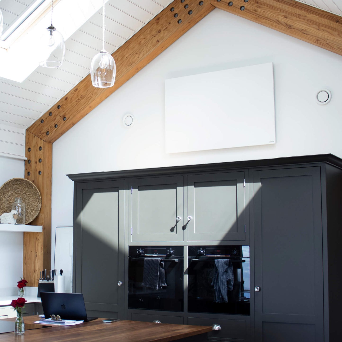 Wit infraroodpaneel gemonteerd aan de wand in een moderne keuken met hoge kasten en houten dakconstructie