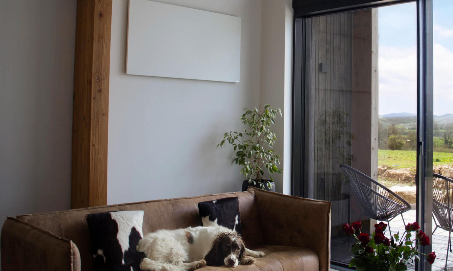 Wit infrarood verwarmingspaneel aan de wand in een woonkamer met sofa en grote raampartij